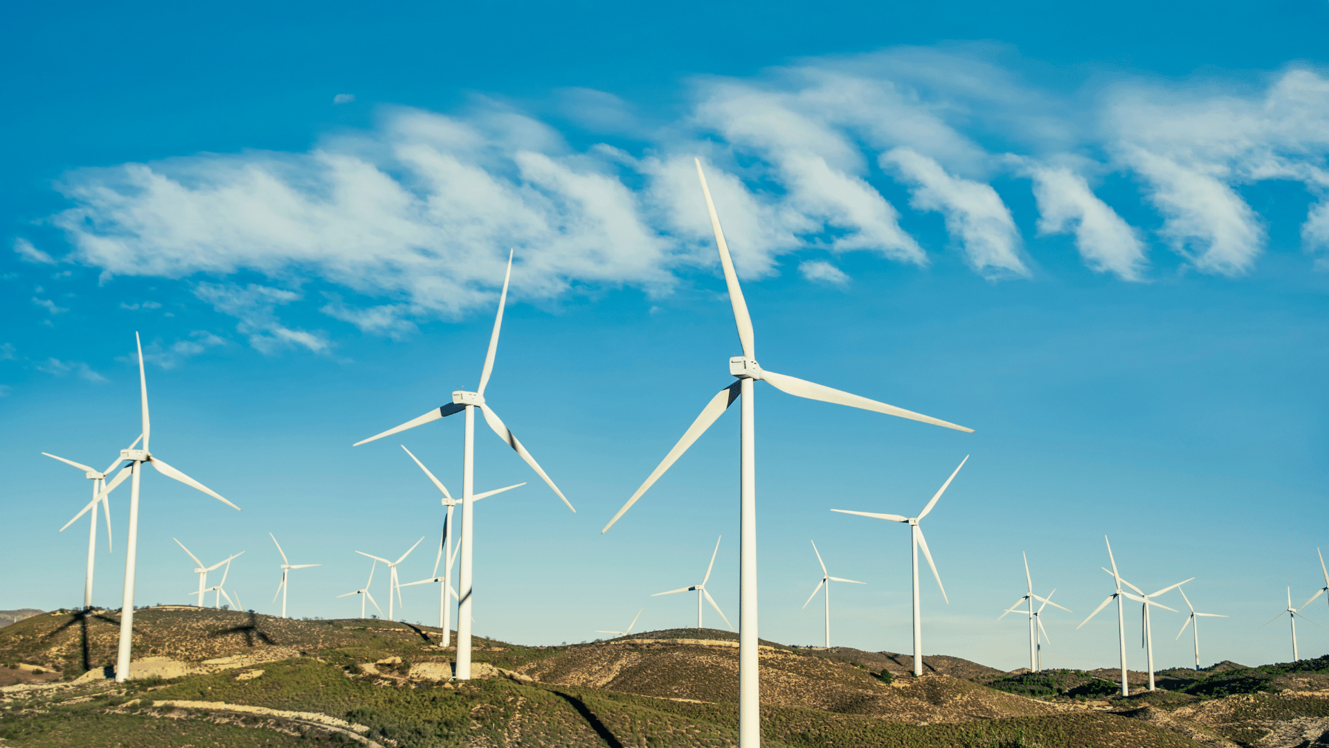 Wind turbines on rolling hills under a blue sky with clouds.