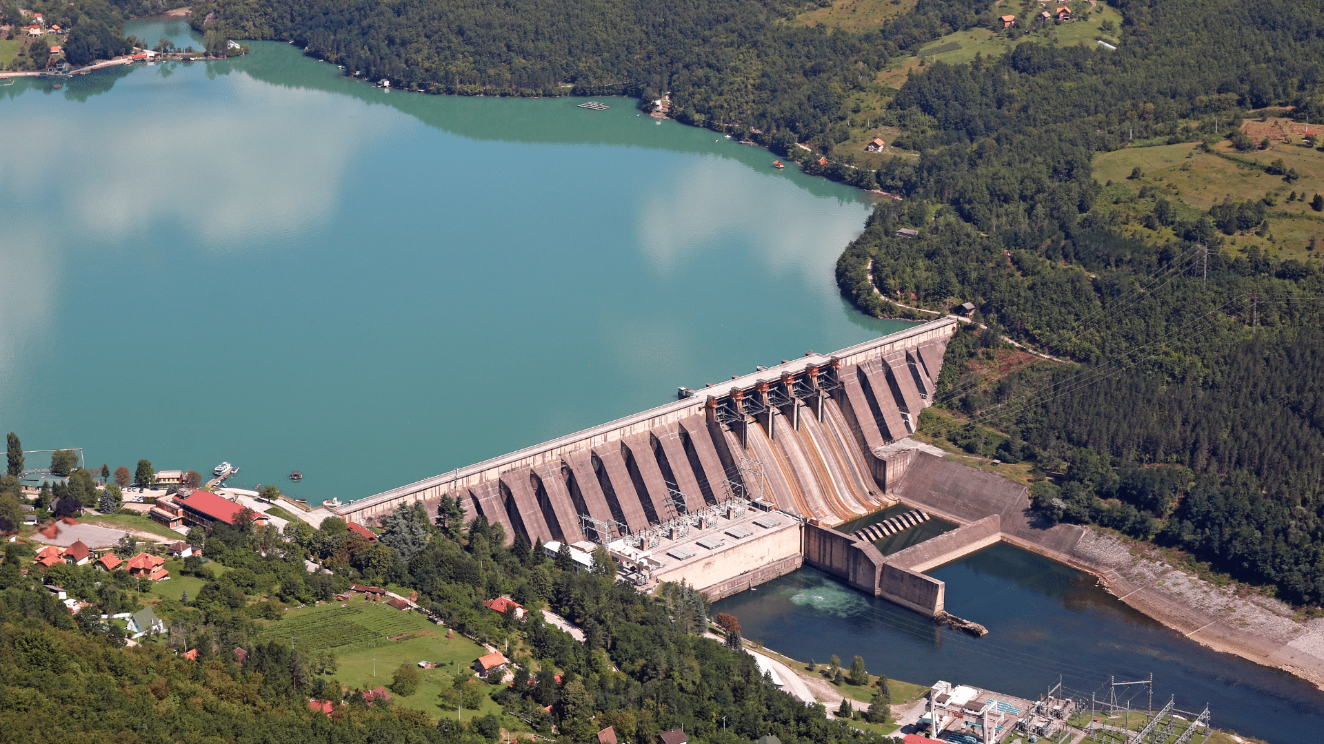 Website blog covers – Energy (3) Aerial view of a large hydroelectric dam with a reservoir and surrounding greenery.