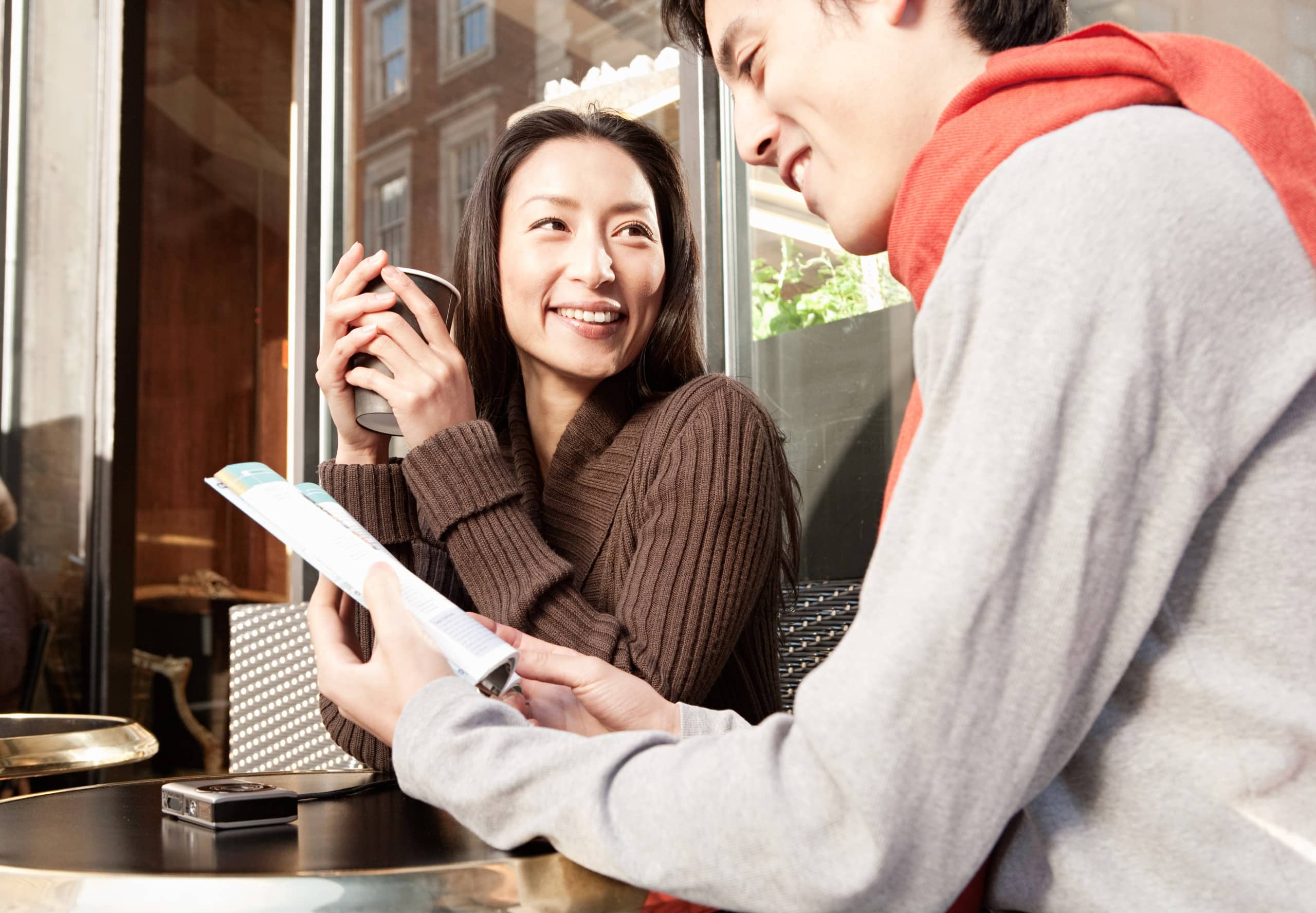 Two people sitting at a café table, smiling and talking over drinks and a menu.