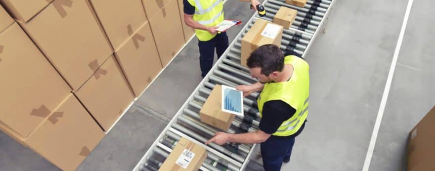 Two warehouse workers scanning cardboard boxes on a conveyer belt