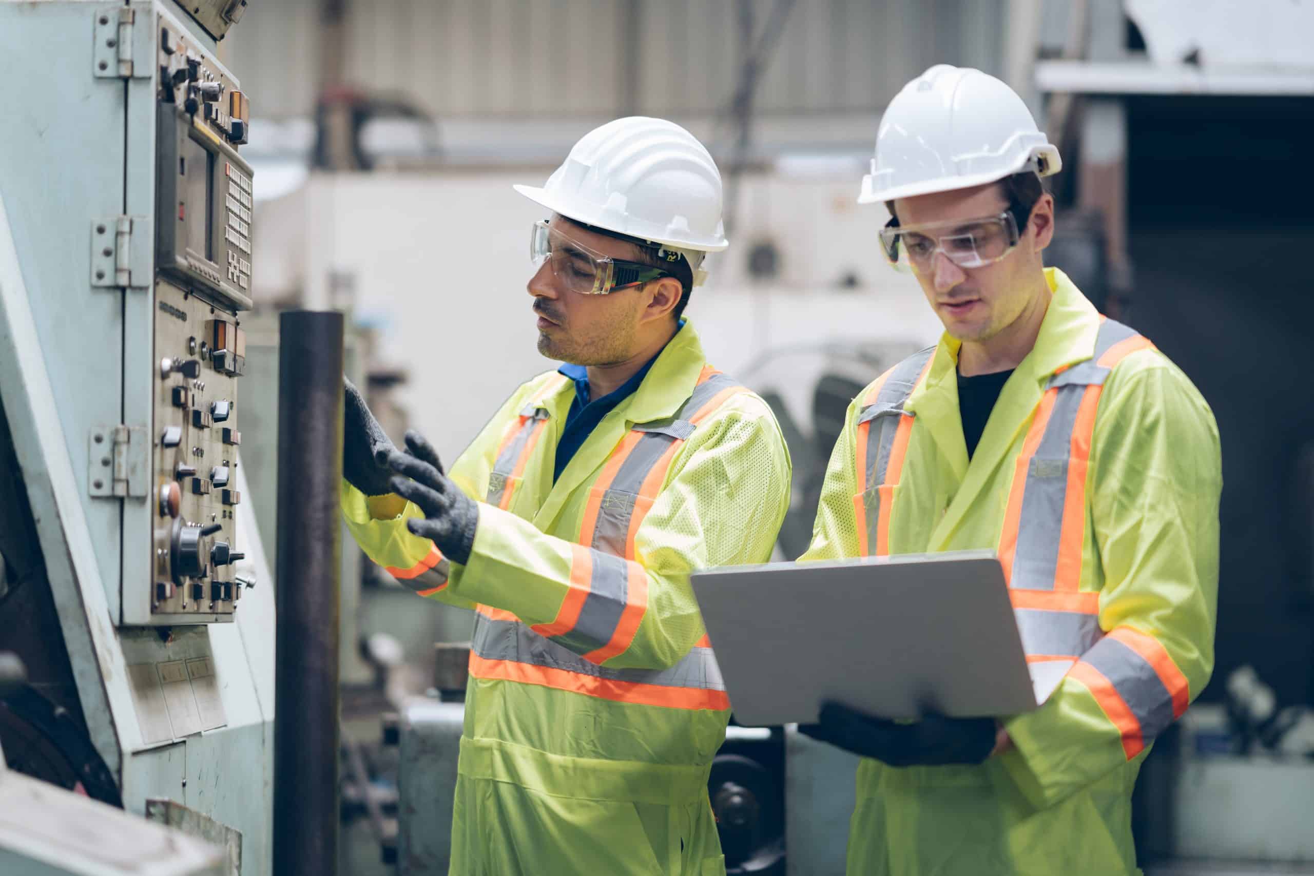 Two workers wearing protective equipment operating machinery