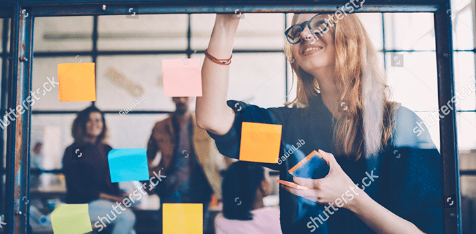 Woman placing sticky notes on glass wall during a team meeting.
