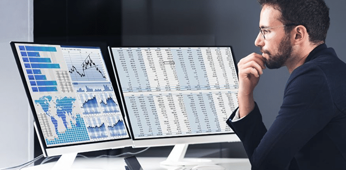 Man analyzing data and charts on two computer monitors in an office.