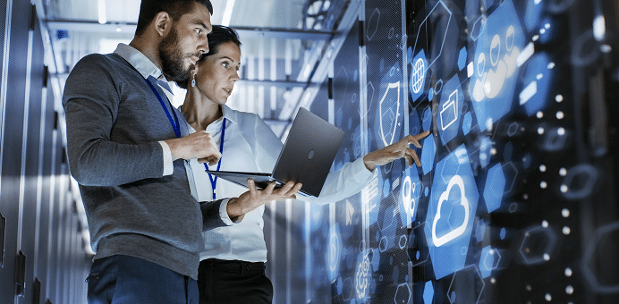 Two people work together on a laptop and touchscreen in a modern server room with digital icons.