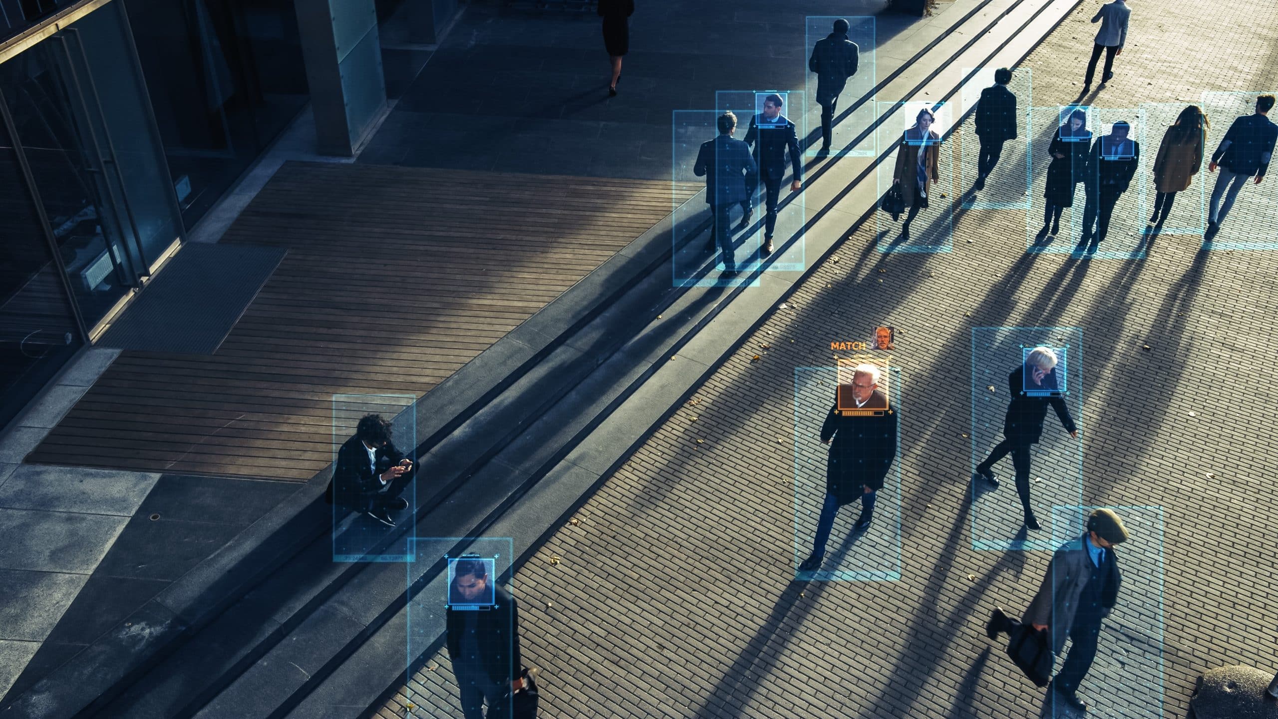 People walking outside, with facial recognition boxes over their heads, shadows on the ground.