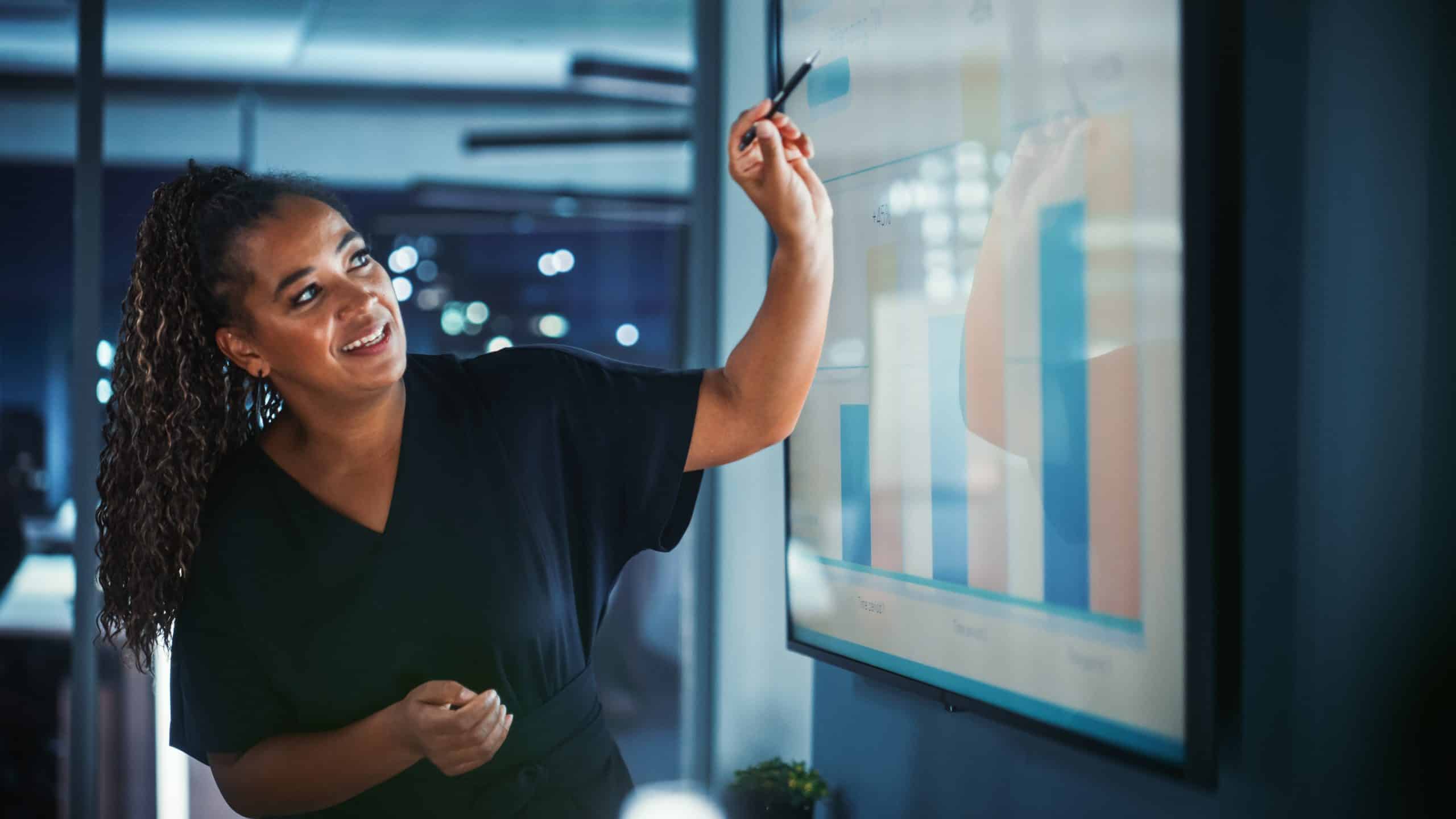 Woman presenting data on a screen with bar charts in an office setting.