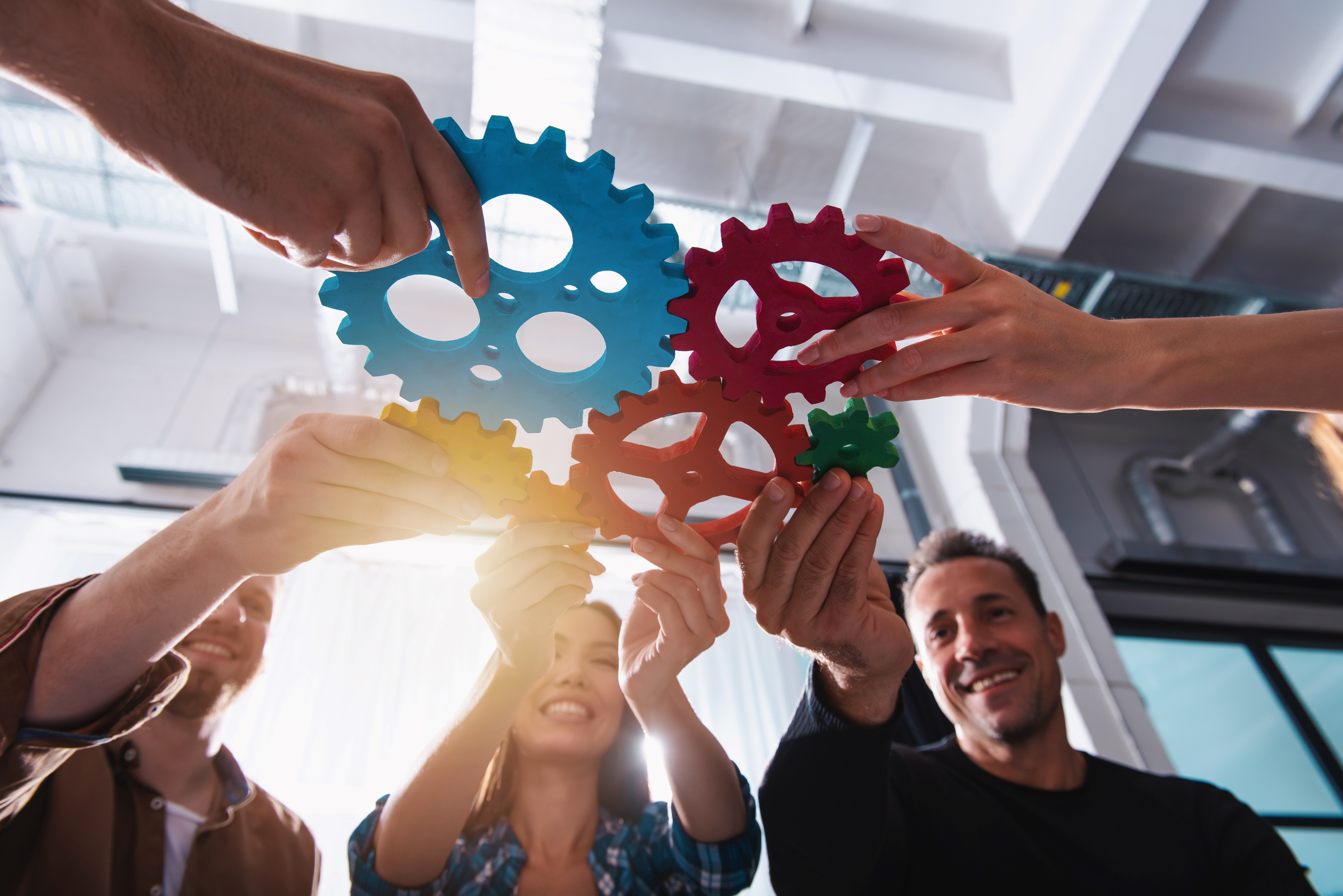 People holding colorful gear pieces together, symbolizing teamwork and collaboration.