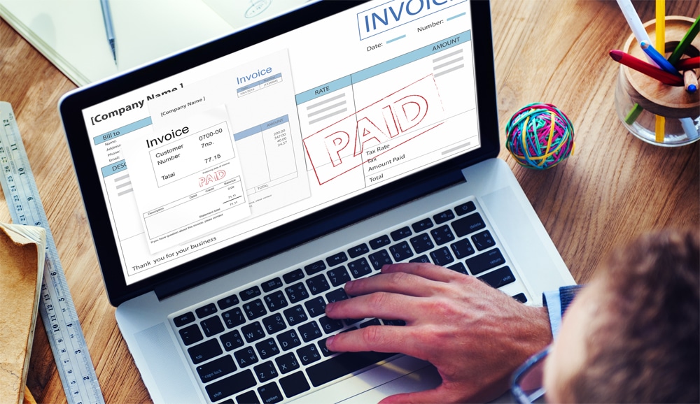 Person using a laptop displaying a paid invoice on the screen.