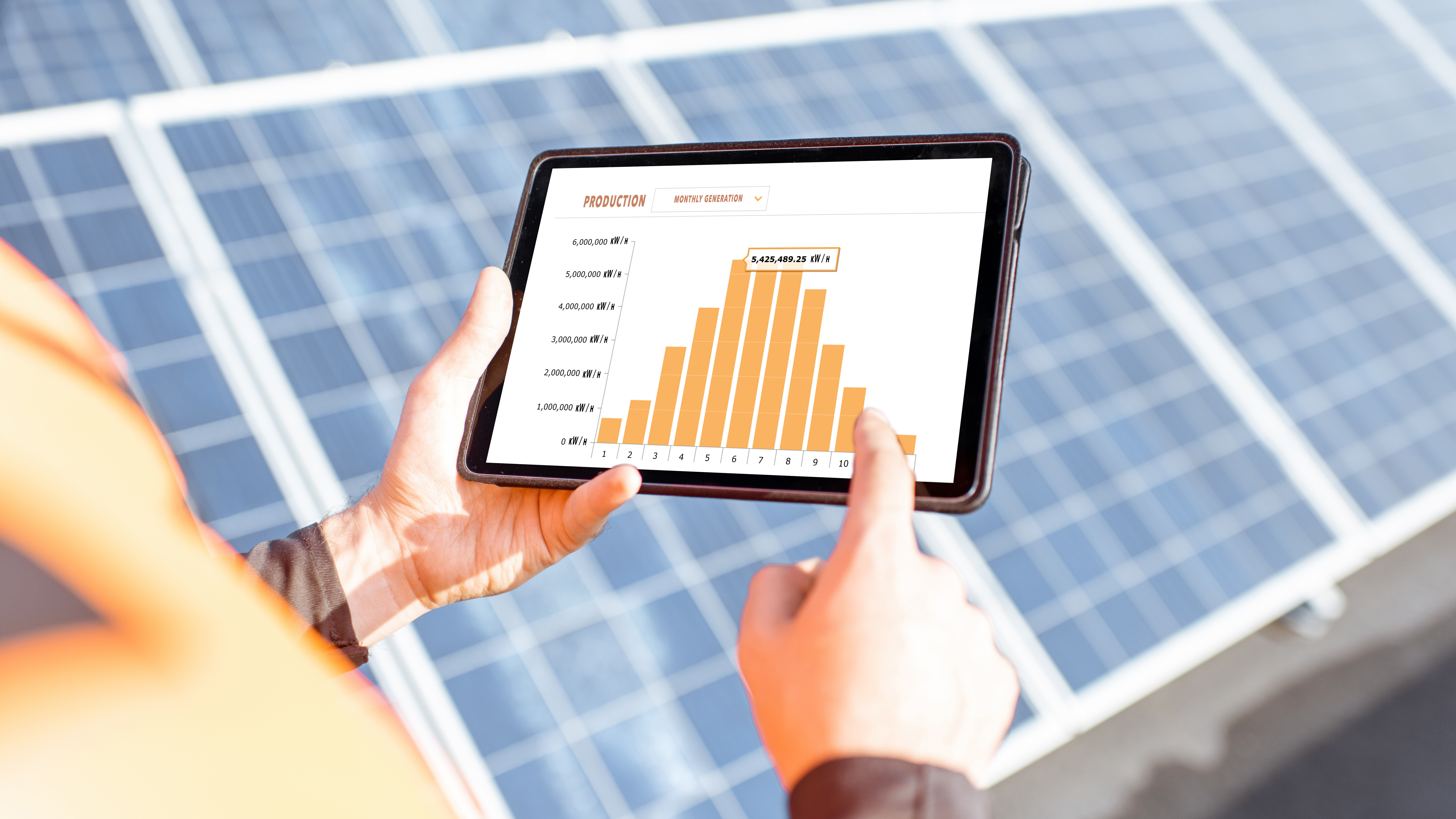 Person holding a tablet with a solar energy production graph, in front of solar panels.