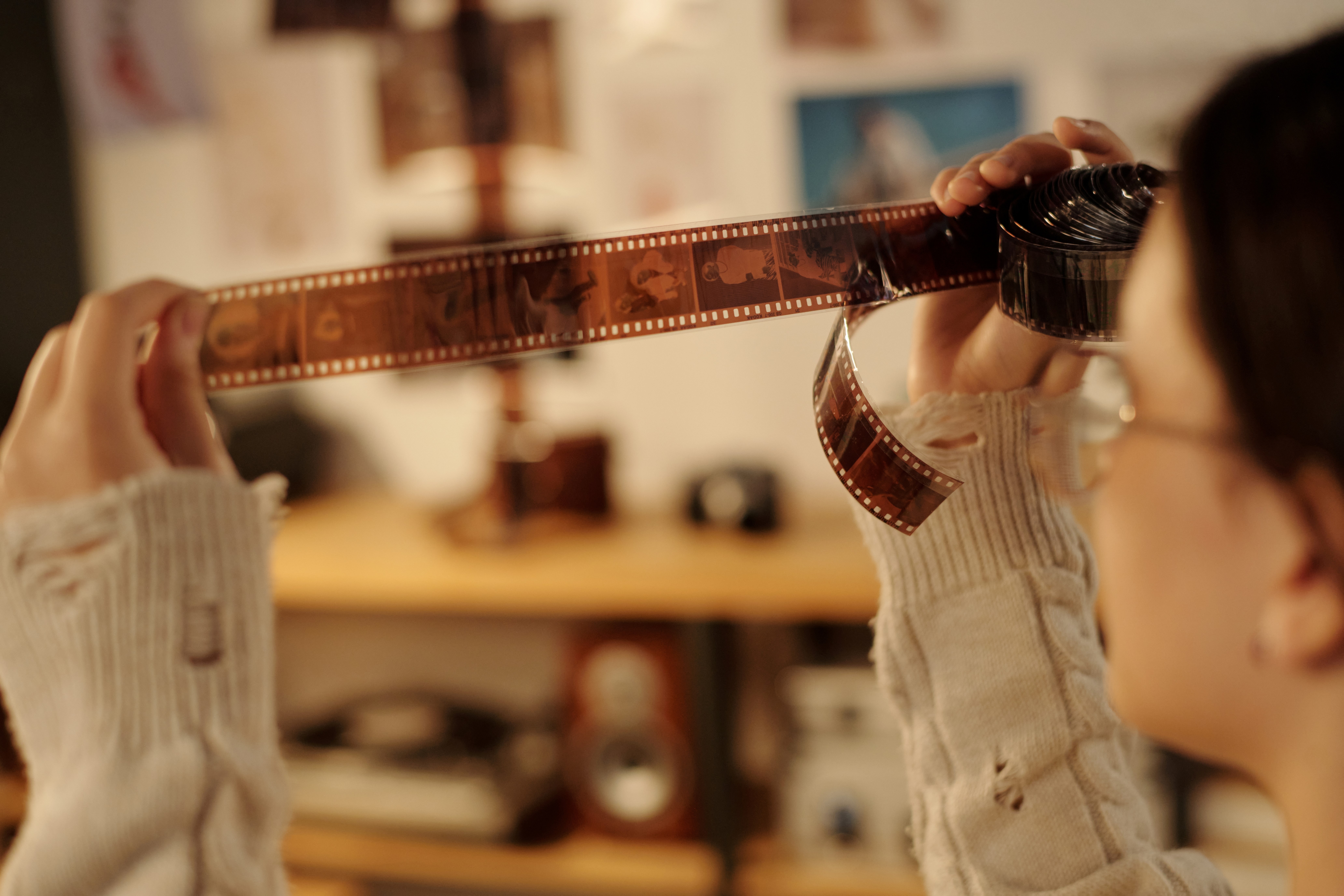 A person holding and examining a strip of photographic film in a room.