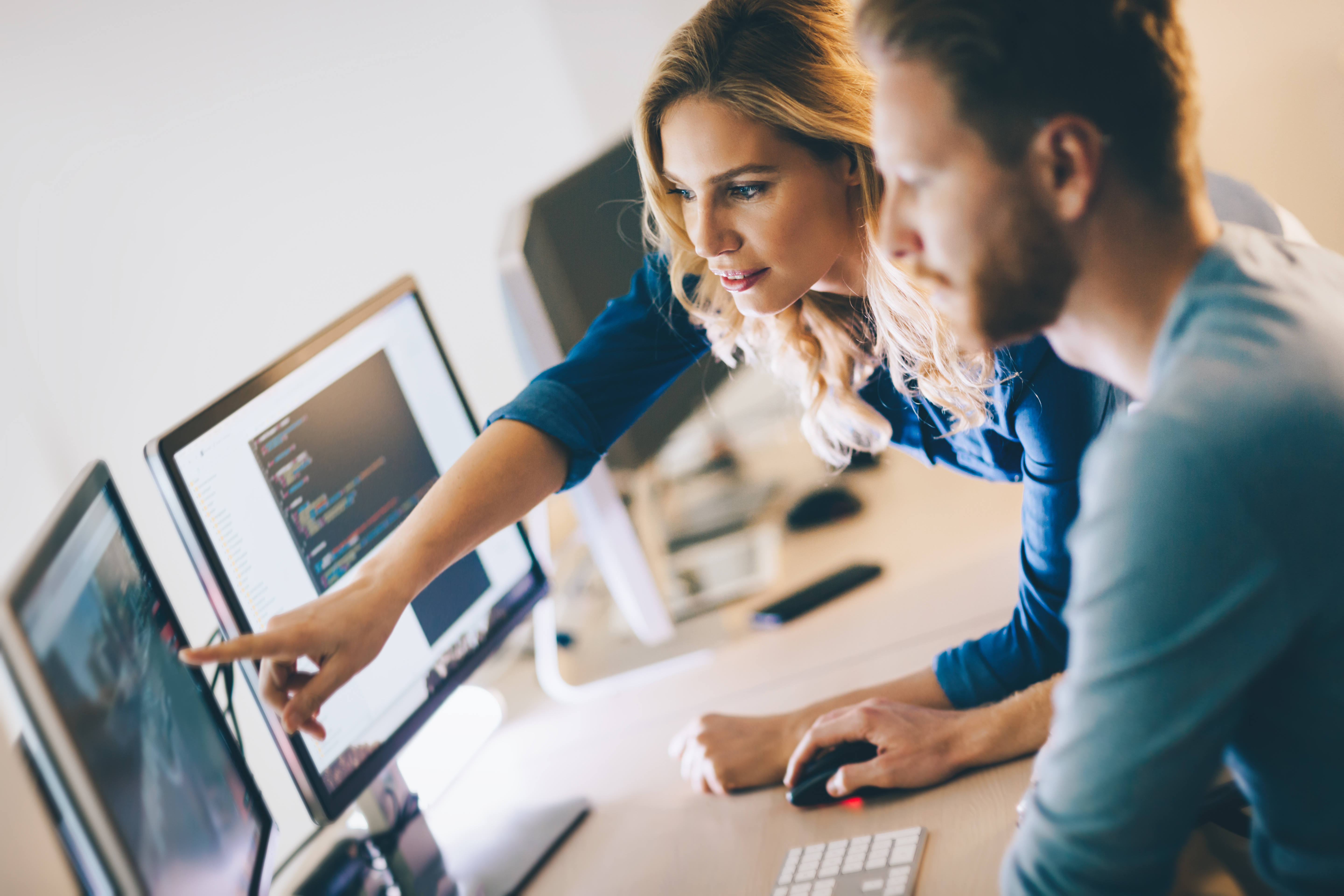 Two people working together at a computer, looking at code on a monitor.