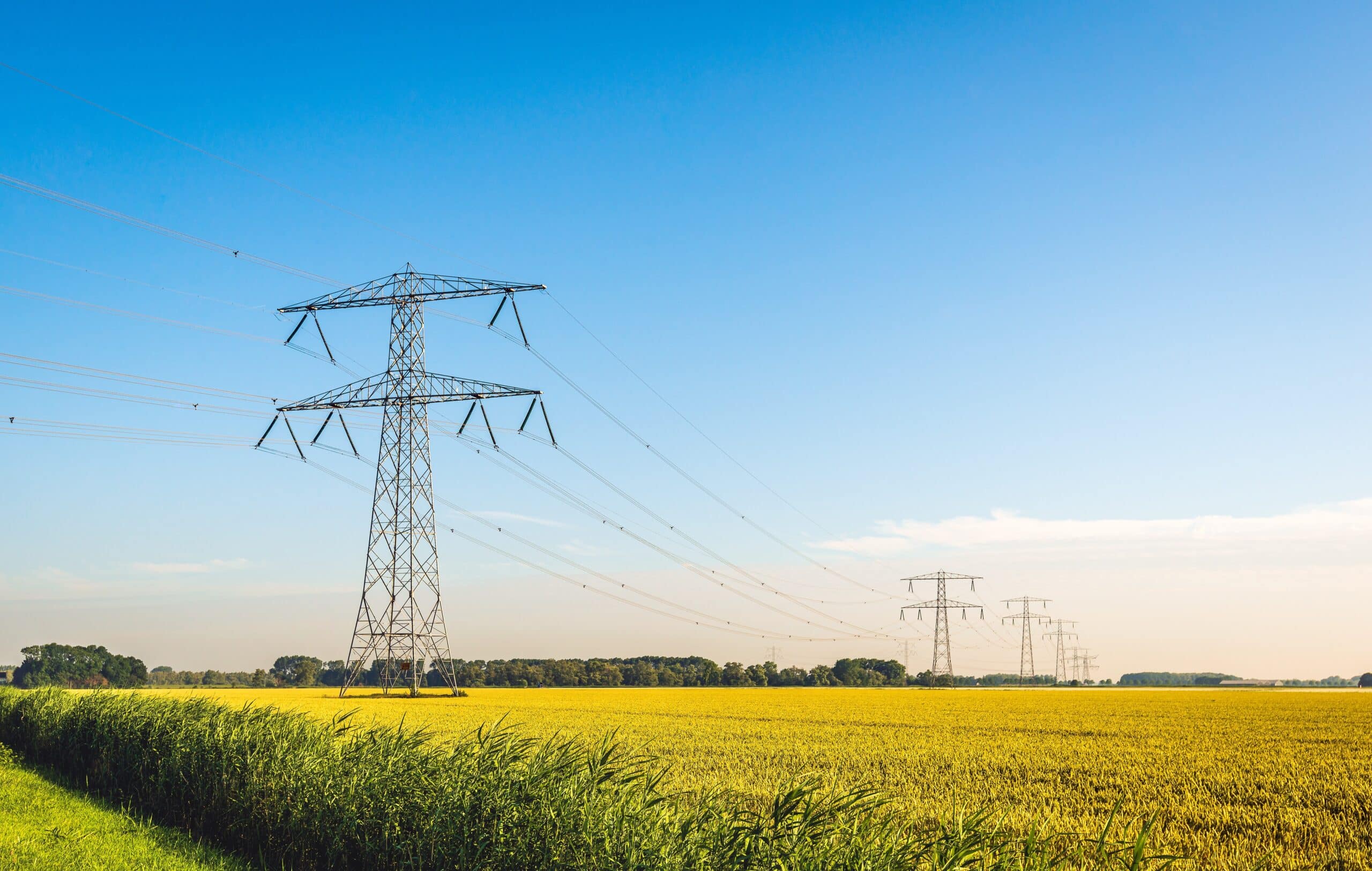 Power lines and transmission towers crossing a field under a clear blue sky.