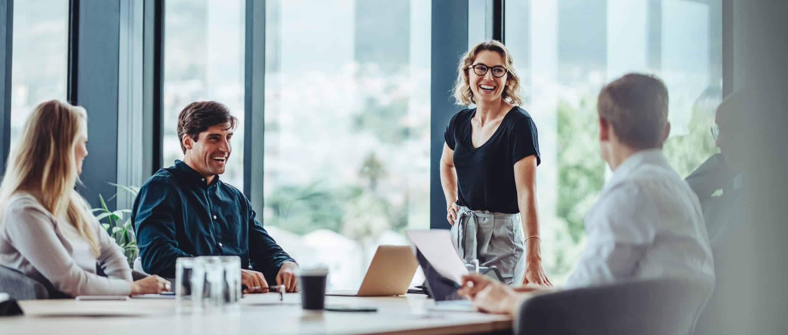 Four people having a meeting in a bright office, with one woman standing and smiling.
