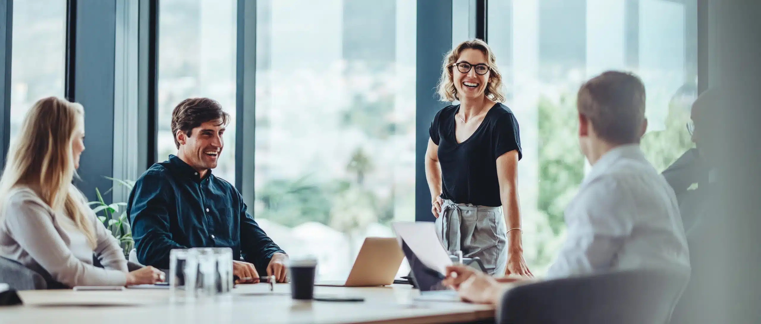 Four people having a meeting in a bright office, with one woman standing and smiling.