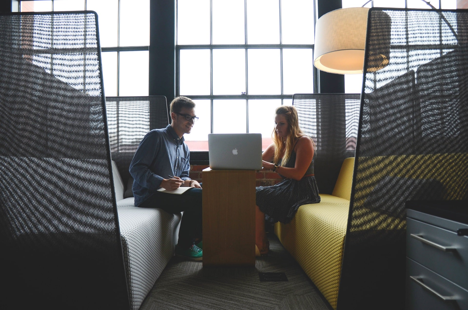 Two people sitting in an office booth working together on a laptop.