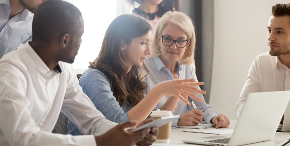 People having a discussion around a table with a laptop and coffee cups.