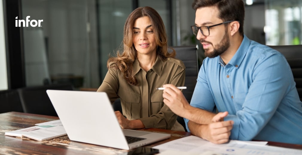 Two people working together at a laptop in an office with documents on the table.