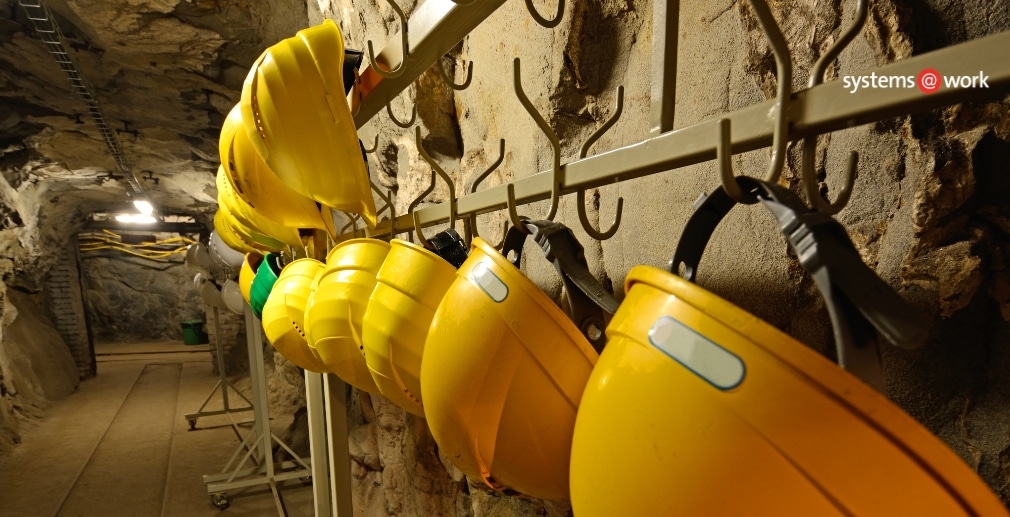 Yellow hard hats hanging on hooks inside an underground tunnel.