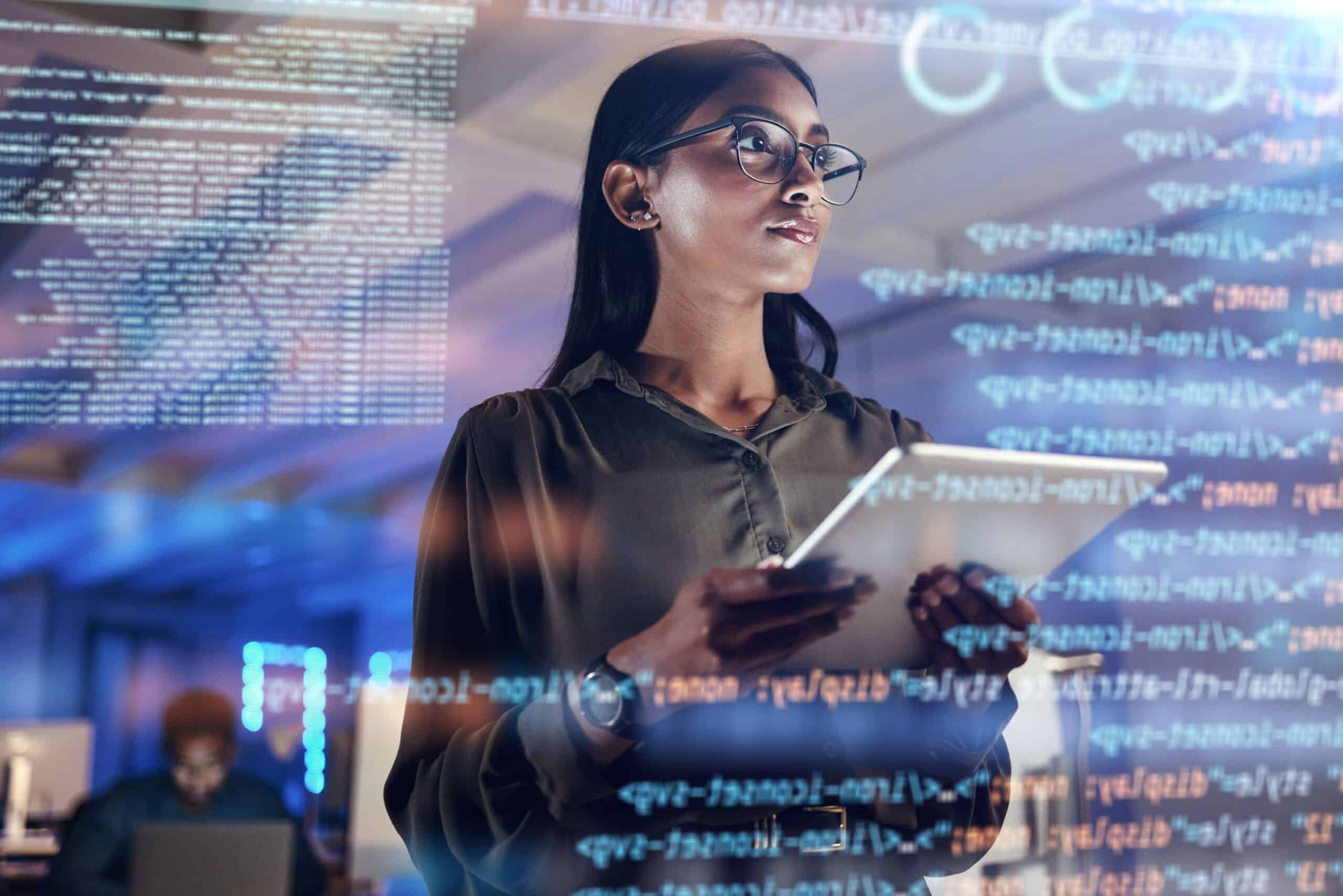 Woman with a tablet analyzing data and code on a transparent screen in an office environment.